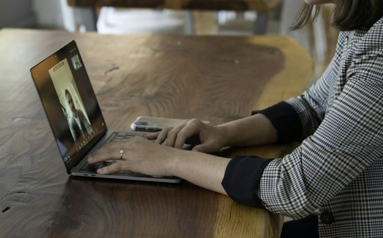 video call Person using a laptop for a video call while sitting at a wooden table.